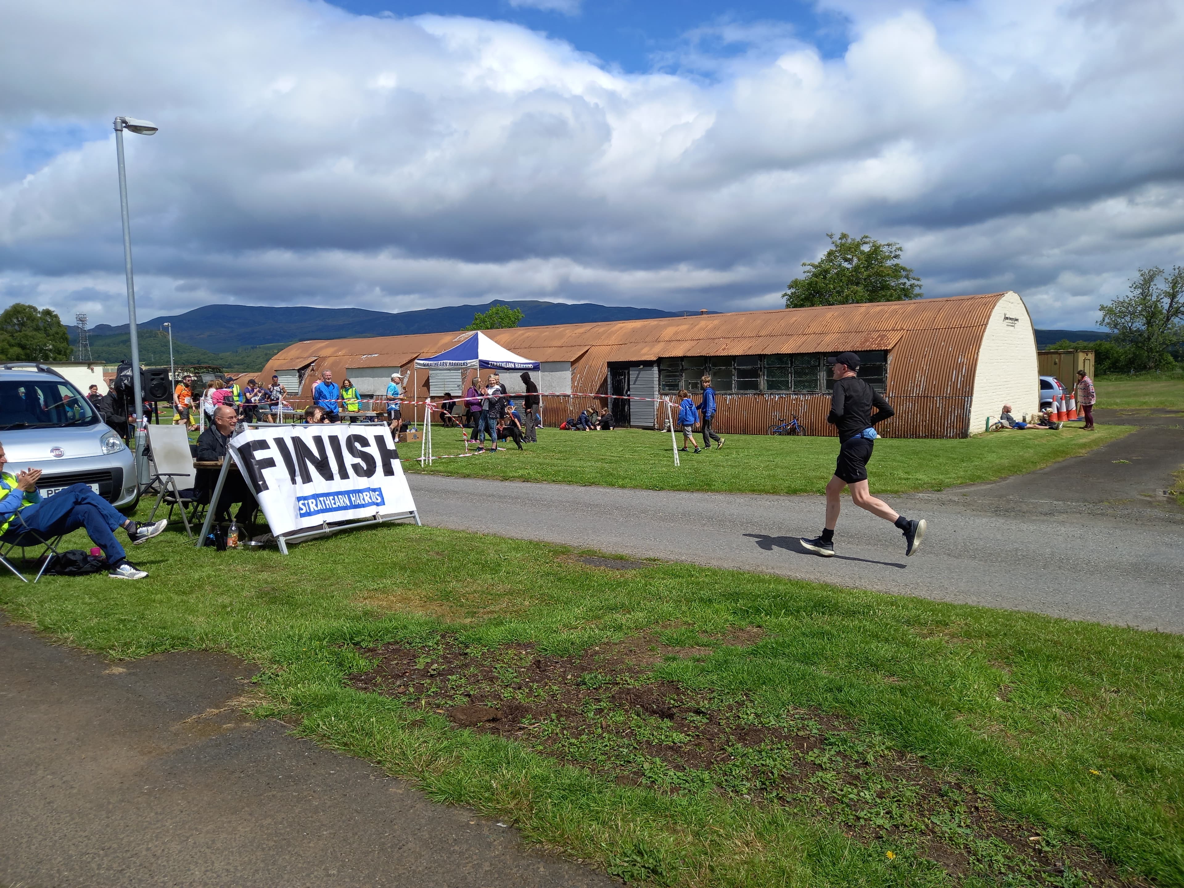 Runner approaching the Strathearn Marathon finish line at Cultybraggan Camp with spectators and Nissen huts nearby