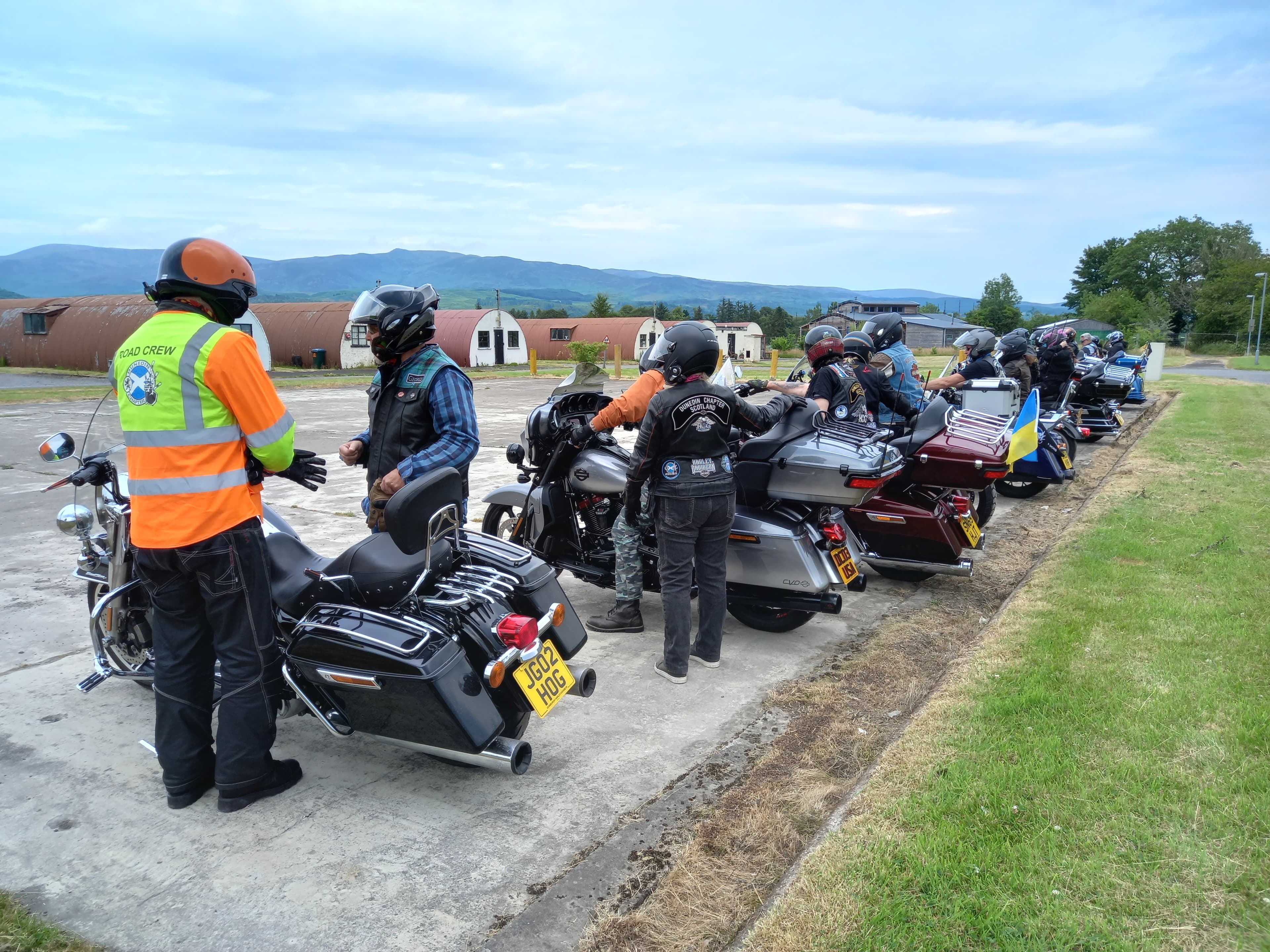 Motorcyclists lined up at Cultybraggan Camp with Nissen huts and Perthshire hills in the background