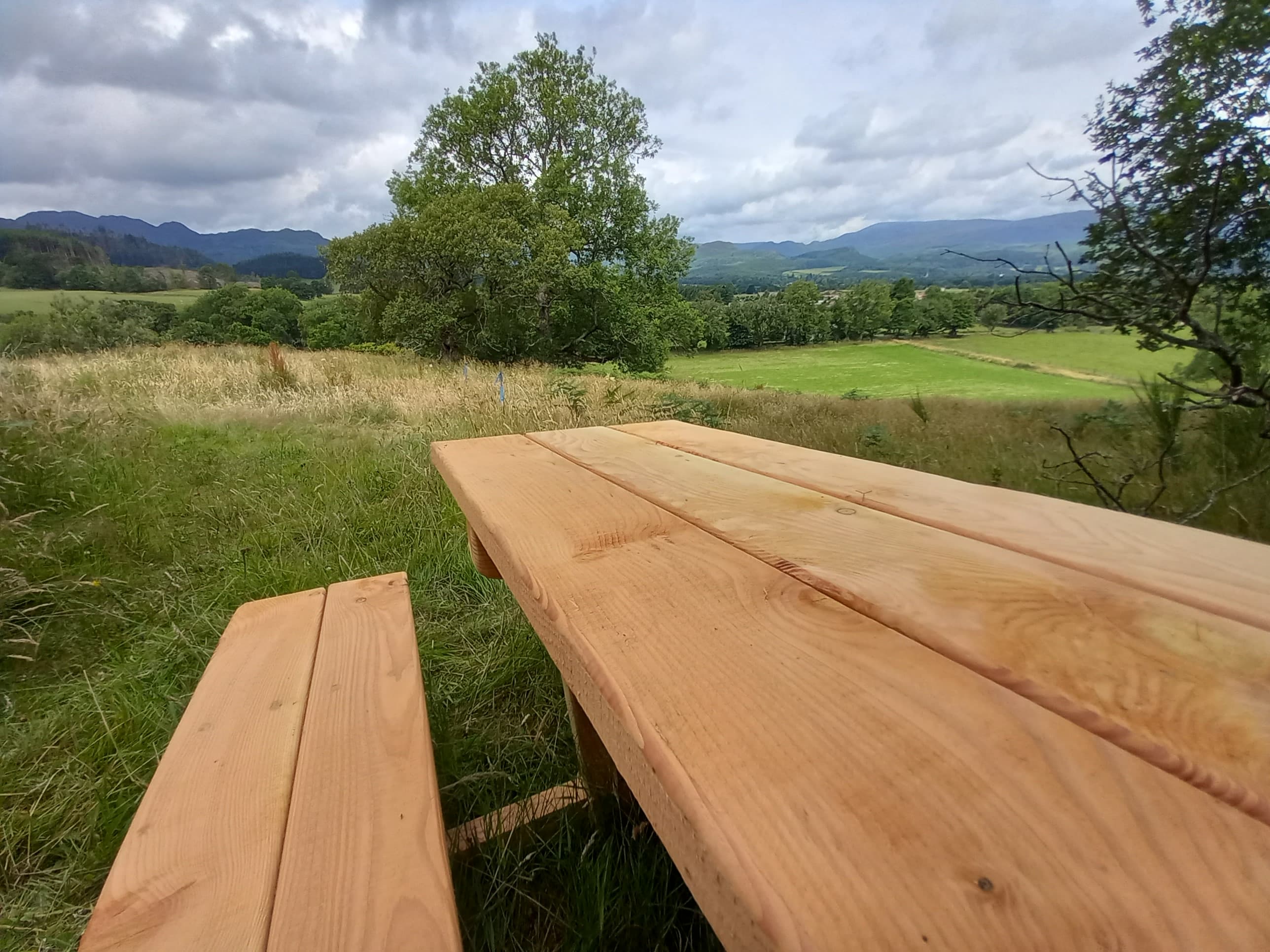 View from a Cultybraggan Camp pitch across picnic seating, green fields, and Perthshire hills